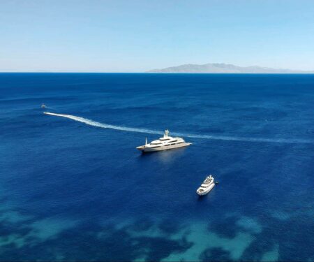 What to Know Before Chartering a Yacht in Greece Luxury yacht anchored in clear blue water near a Greek island in the Cyclades