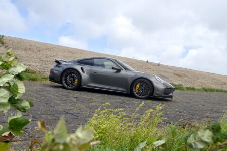 Porsche’s New 911 Turbo S Makes 711bhp Feel Remarkably Usable Porsche 911 Turbo S 992.2 driving on a road with wide rear arches and fixed rear wing visible