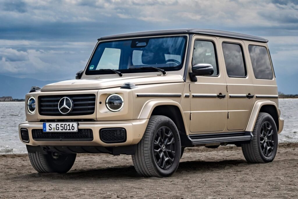 Smaller Mercedes-Benz G-Class inspired SUV on a rugged road near a modern European factory