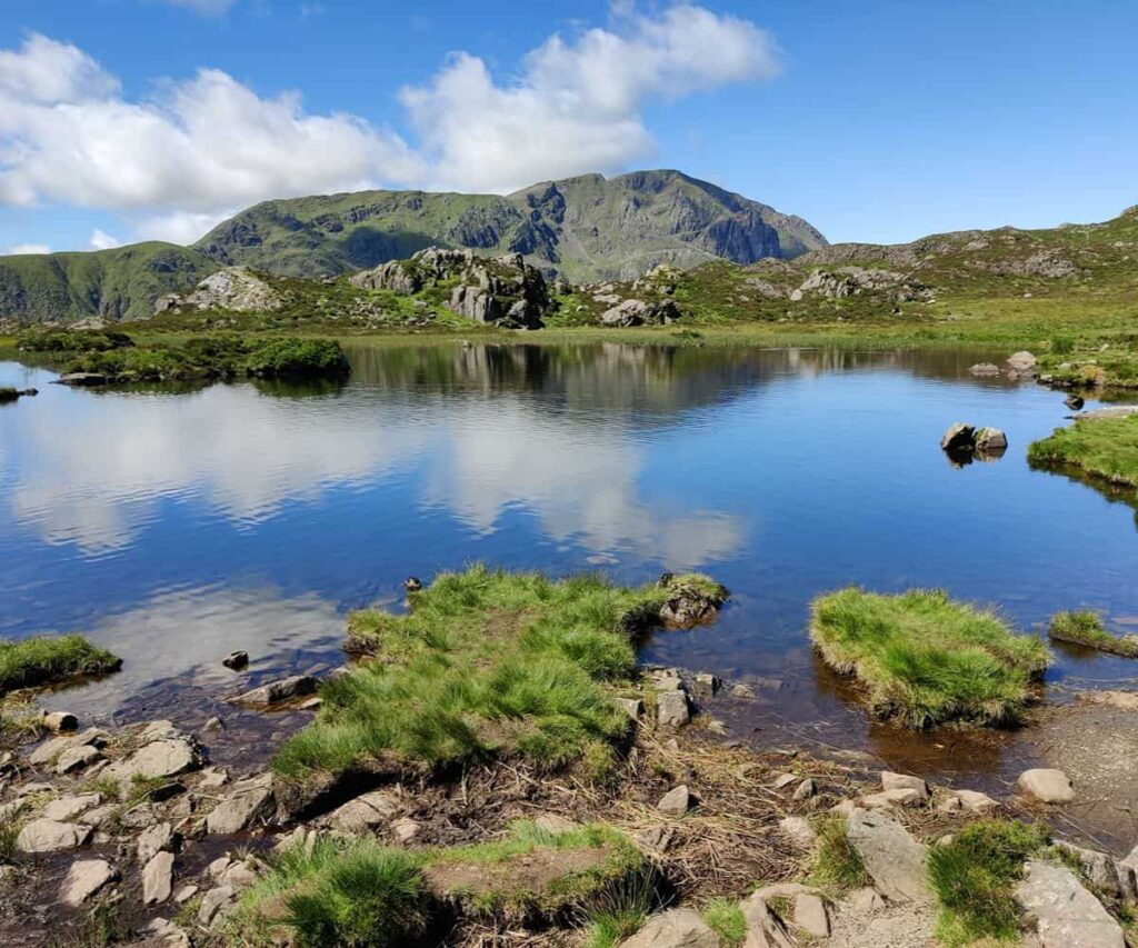 10 Cool Things to Do in the Lake District When the Temperature Rises A calm Lake District shoreline in summer with mountains in the distance