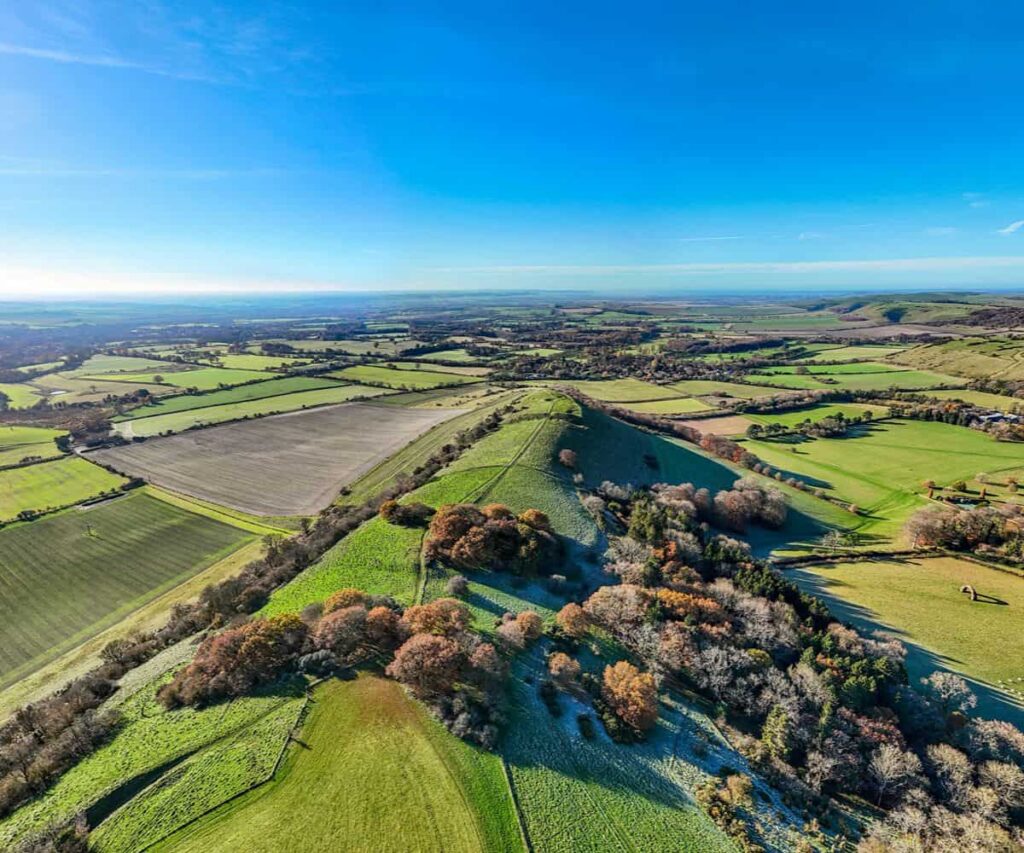 Rolling Wiltshire countryside with chalk hills and a historic village in warm evening light