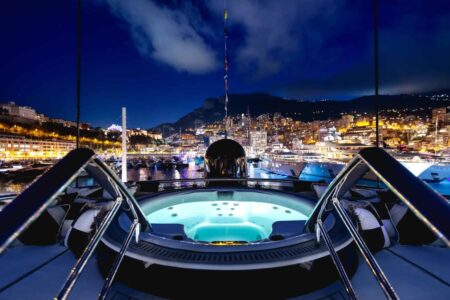 Modern superyacht anchored in a calm bay with open decks and a beach club at the stern
