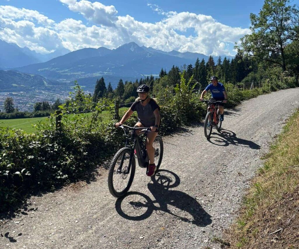 Exploring Innsbruck by E-Mountain Bike Turns the Nordkette Into a Family Ride E-mountain bikes on a forest trail above Innsbruck with Alpine pastures and the Nordkette mountains nearby