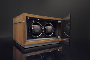 Watch accessories including a leather watch case, watch winder, custom straps and laptop corner protection arranged on a desk